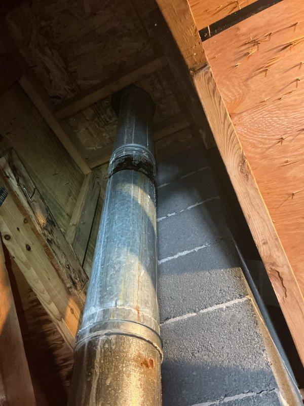 Responded to service call regarding home inspector's report of cracked exhaust pipe in attic space. Inspected 6-year-old water heater exhaust vent system running through attic and wall cavity. Upon visual inspection, identified discoloration on lower section of metal vent pipe but found no visible cracks or separation at joints. Photographed vent pipe installation showing proper vertical routing through wooden framing members with appropriate clearances. Exhaust system appears structurally intact with all connections secure. Documented condition for client records.