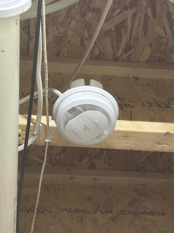 Responded to address improper installation from previous service call where CO-only alarms were installed instead of combination CO/smoke detectors, leaving exposed wiring and disconnected units. Removed incorrectly installed CO-only alarms and installed proper combination CO and smoke detector units in unfinished ceiling areas, securing all electrical connections and eliminating exposed wiring hazards. Verified all replacement alarms were functioning properly with indicator lights operational.