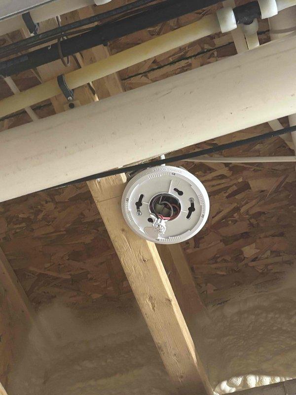 Responded to address improper installation from previous service call where CO-only alarms were installed instead of combination CO/smoke detectors, leaving exposed wiring and disconnected units. Removed incorrectly installed CO-only alarms and installed proper combination CO and smoke detector units in unfinished ceiling areas, securing all electrical connections and eliminating exposed wiring hazards. Verified all replacement alarms were functioning properly with indicator lights operational.