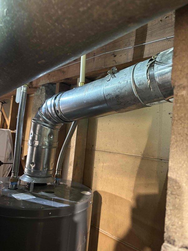 Corrected water heater venting installation to meet code requirements by relocating new vent pipe to maintain proper clearance from SharkBite flexible water connectors. Repositioned metallic ductwork and secured with appropriate hangers and strapping to wooden ceiling joists, ensuring adequate separation between venting system and plumbing connections as required by municipal inspection standards.