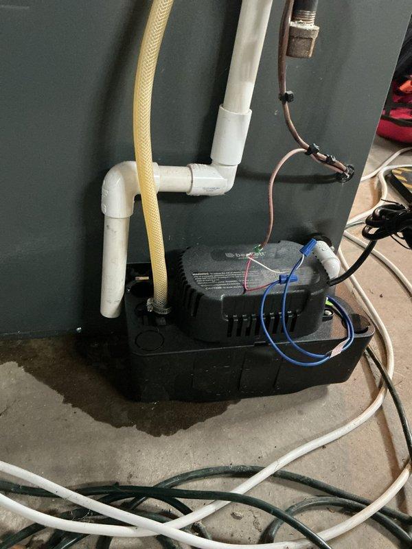 Responded to service call for leaking furnace at residential property with 10-year-old EnergiAir unit. Upon inspection, identified water leak originating from condensate drainage system. Inspected condensate pump installation, PVC drain lines, and associated plumbing connections against basement wall. Documented existing pump setup with white PVC vertical drainage piping, flexible discharge hose, and electrical connections showing moisture accumulation on concrete floor around pump unit. Photographed complete condensate management system to assess leak source and verify proper pump operation for heating system functionality.