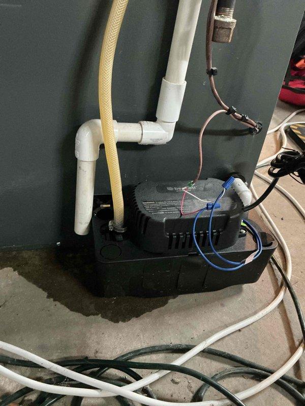 Responded to service call for leaking furnace at residential property with 10-year-old EnergiAir unit. Upon inspection, identified water leak originating from condensate drainage system. Inspected condensate pump installation, PVC drain lines, and associated plumbing connections against basement wall. Documented existing pump setup with white PVC vertical drainage piping, flexible discharge hose, and electrical connections showing moisture accumulation on concrete floor around pump unit. Photographed complete condensate management system to assess leak source and verify proper pump operation for heating system functionality.