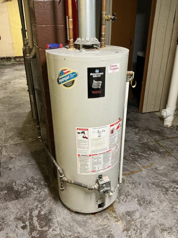 Responded to water heater leak complaint on 10+ year old Bradford White residential unit. Upon inspection, confirmed active leak originating from bottom of tank, indicating internal tank failure typical of units exceeding expected service life. Documented existing conditions with photographs showing water heater installation in basement utility area with visible floor staining and discoloration around base of unit. Assessed all plumbing connections, copper supply lines, and surrounding infrastructure. Advised customer that tank replacement is necessary as bottom leaks cannot be repaired and pose risk of catastrophic failure and water damage. Unit showing age-related deterioration consistent with end of service life expectancy.