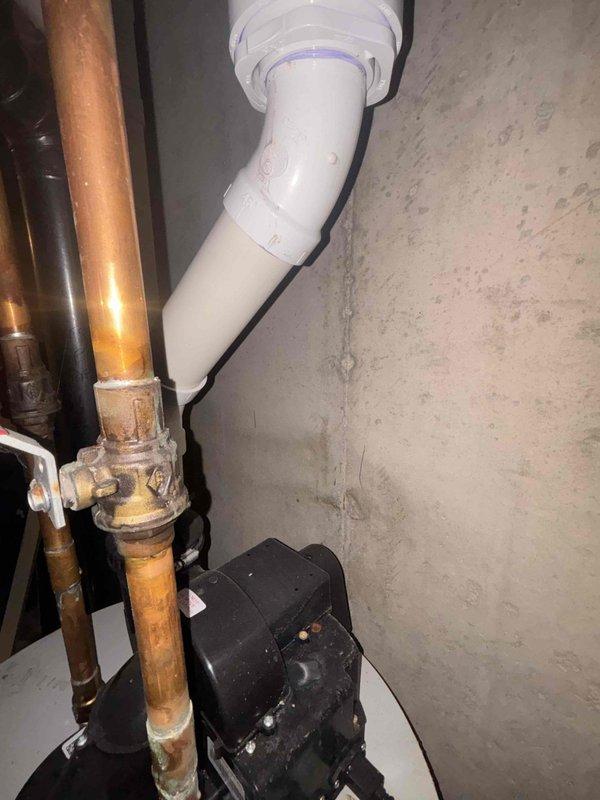 Responded to plumbing lead for leaking water softener system. Upon inspection, identified leak originating from water softener installation consisting of dual-tank Bayes system with tall brine tank and shorter resin tank. Examined copper supply piping with red-handled shut-off valves and connections to treatment system. Assessed aging copper piping showing corrosion and patina, along with newer PVC drainage components. Documented existing plumbing configuration including pump unit and electrical connections for water treatment system. Photographed installation to record current condition of equipment, piping connections, and potential leak sources for repair recommendations.
