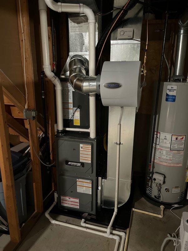 Completed full HVAC system installation including new furnace and air conditioning condenser unit. Installed outdoor AC condenser on concrete pad against exterior wall with proper refrigerant line routing secured to house exterior via mounting brackets. Indoor installation included new furnace in basement mechanical room with complete white PVC venting system, integrated Aprilaire whole-house humidifier, and all necessary ductwork connections. All equipment installed per manufacturer specifications with proper electrical connections, condensate drainage, and gas piping. System tested and verified operational upon completion.