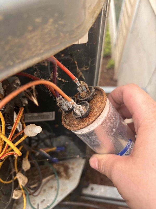 Responded to no cooling condition affecting entire residence with 10-year-old air conditioning system. Upon inspection, discovered failed dual run capacitor exhibiting severe corrosion and terminal deterioration. Performed electrical diagnostics using digital multimeter to confirm capacitor failure with zero microfarad reading. Removed and replaced defective capacitor with new OEM-equivalent component. Verified proper electrical connections, tested system operation, and confirmed restoration of cooling to all areas of home. Unit returned to normal operating parameters.