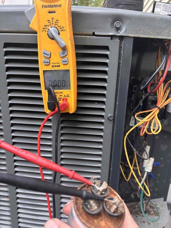 Responded to no cooling condition affecting entire residence with 10-year-old air conditioning system. Upon inspection, discovered failed dual run capacitor exhibiting severe corrosion and terminal deterioration. Performed electrical diagnostics using digital multimeter to confirm capacitor failure with zero microfarad reading. Removed and replaced defective capacitor with new OEM-equivalent component. Verified proper electrical connections, tested system operation, and confirmed restoration of cooling to all areas of home. Unit returned to normal operating parameters.