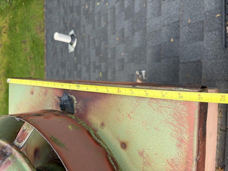 Responded to water leak complaint originating from flue system penetration at roof level. Upon inspection, identified previous amateur patch repair that had failed, allowing water intrusion during rain events. Documented existing conditions with photographs showing corroded flue components with significant oxidation and deterioration of metal surfaces. Measured affected area and assessed structural integrity of flue assembly and surrounding roofing materials. Flue pipe exhibited advanced corrosion with rust patina and surface pitting, indicating prolonged exposure to moisture. Roofing substrate around penetration showed water staining and weathering. Insulation wrap at base of flue component appeared compromised. Recommended complete flue system replacement rather than additional patching due to extent of corrosion and age of existing components to ensure permanent resolution of leak issue.