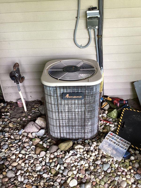# AC No Cooling - 16 Year Old Amana System

Responded to service call for air conditioning system not cooling properly. Upon arrival, inspected 16-year-old Amana outdoor condensing unit located on exterior of residence.

**Inspection Findings:**
- Outdoor unit accessible with electrical disconnect and refrigerant lines properly installed
- Significant deterioration observed inside electrical compartment
- Extensive rust staining, dirt accumulation, and debris buildup throughout interior housing
- Capacitor and wiring connections inspected - multiple colored wire terminals present on cylindrical capacitor
- Evidence of moisture intrusion and environmental exposure causing interior component degradation

**Work Performed:**
- Performed visual inspection of outdoor condensing unit
- Opened electrical compartment to assess internal components
- Documented condition of capacitor, wiring, and interior housing
- Photographed equipment condition for service records
- Assessed overall system de