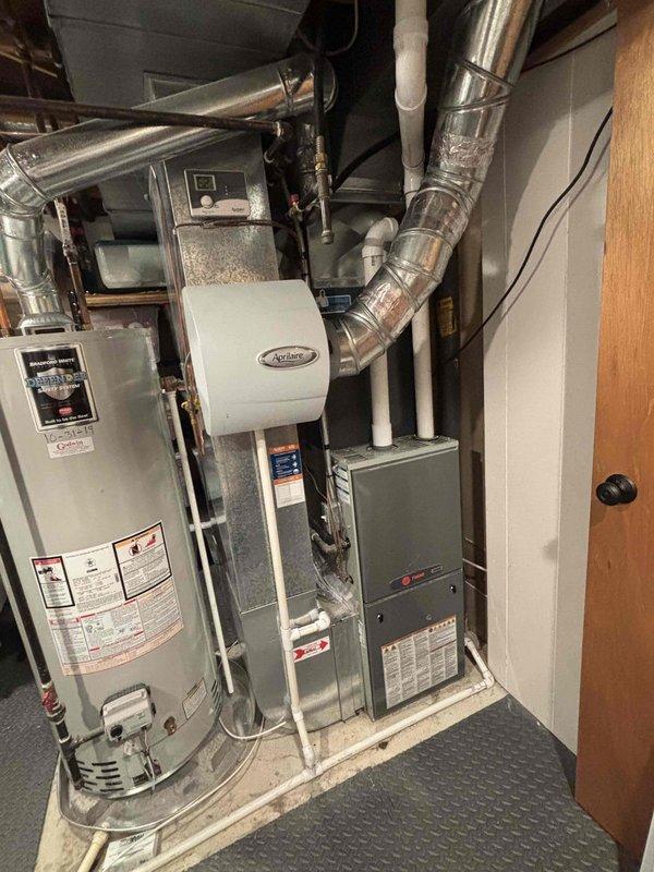 Completed full HVAC system replacement including furnace and air conditioning unit in basement utility room. Installed new gray metal furnace with proper electrical connections and ventilation, along with coordinating air conditioning equipment. System integration included existing Aprilaire humidifier with metallic ductwork connections, ensured all components properly configured and operational with standard residential water heater remaining in place.