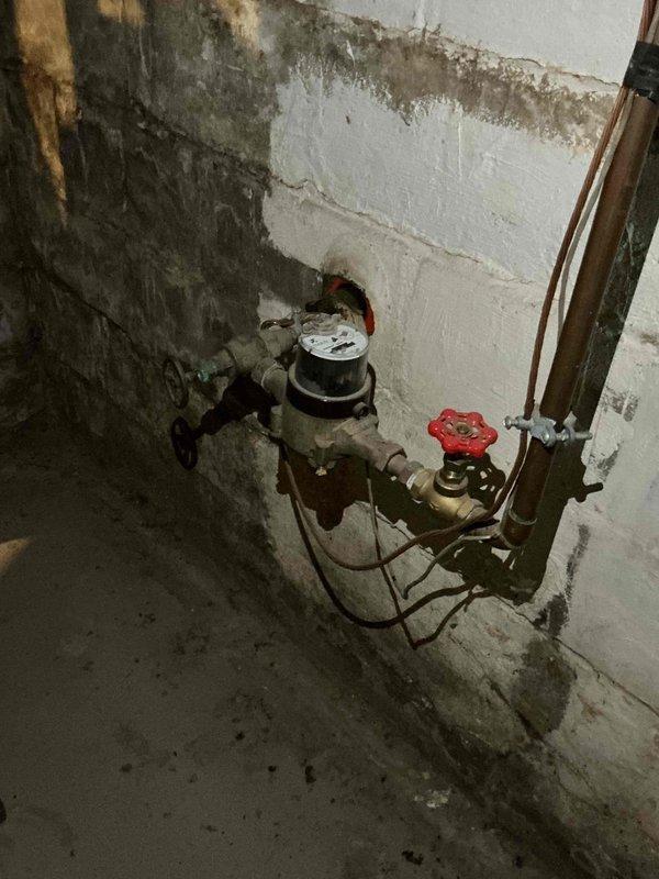 Conducted comprehensive plumbing project estimate for basement utility work including installation of new utility sink, replacement of deteriorated outdoor spigot, and assessment of additional minor plumbing tasks. Documented existing conditions showing aged copper piping with gate valves and water meter assembly in basement corner area with significant moisture damage to concrete block walls. Evaluated workspace constraints including exposed fiberglass insulation, HVAC ductwork, and limited access conditions typical of unfinished basement mechanical areas.