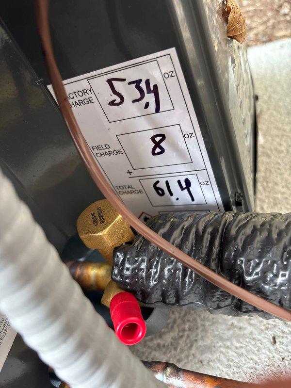 Completed add-on air conditioning system installation at residential property. Installed new outdoor condensing unit on concrete pad adjacent to house exterior, secured refrigerant lines to siding with proper routing, and mounted electrical disconnect box. Charged system with refrigerant per manufacturer specifications, documenting factory charge of 534 oz and field charge of 8 oz for total system charge of 61.4 oz. Verified all refrigerant connections, service ports, and line insulation properly installed. System tested and operational.