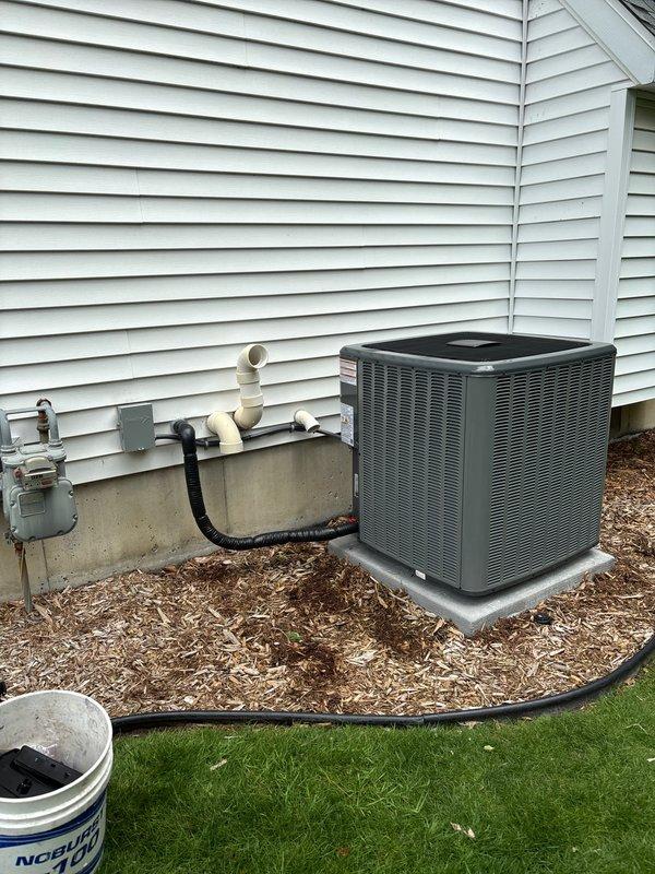 Successfully completed full air conditioning system replacement at residential property. Installed new condensing unit on existing concrete pad with proper electrical disconnect, refrigerant line connections using brass service valves with protective caps, and integrated PVC drainage system along foundation. All refrigerant lines properly insulated, system tested and verified operational, with unit positioned on stable pad surrounded by landscaped mulch bed for optimal airflow and drainage.