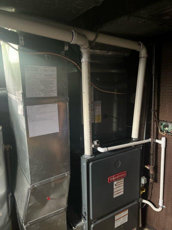 Completed full residential air conditioning system replacement in basement utility area. Removed existing HVAC equipment and installed new Coleman furnace unit with matching air handler featuring light blue-green metallic exterior casing. Configured complete refrigerant line set with copper tubing wrapped in black insulation material, running vertically along wall from outdoor condenser to indoor coil. Installed white PVC condensate drainage system with multiple elbows and connections, properly secured to ceiling with mounting brackets. Connected all electrical wiring and control circuits between components. Verified proper refrigerant charge and system pressures. Tested all safety controls, thermostatic operation, and airflow performance. System operational and performing to manufacturer specifications upon completion.