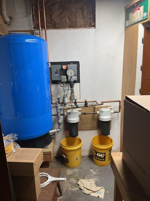 Responded to water leak from pressure relief valve on water heater. Upon arrival, confirmed active discharge from temperature and pressure relief valve on Bradford White replacement unit installed in 2020 with warranty expiration October 2033. Inspected water heater installation, associated copper piping connections, and surrounding plumbing system including pressure tank and dual water filtration housings. Documented existing conditions with photographs showing utility area setup, wall staining from previous moisture exposure, and complete mechanical room configuration. Assessed PRV operation and system pressure to determine cause of discharge and recommended appropriate corrective action to resolve leak condition.