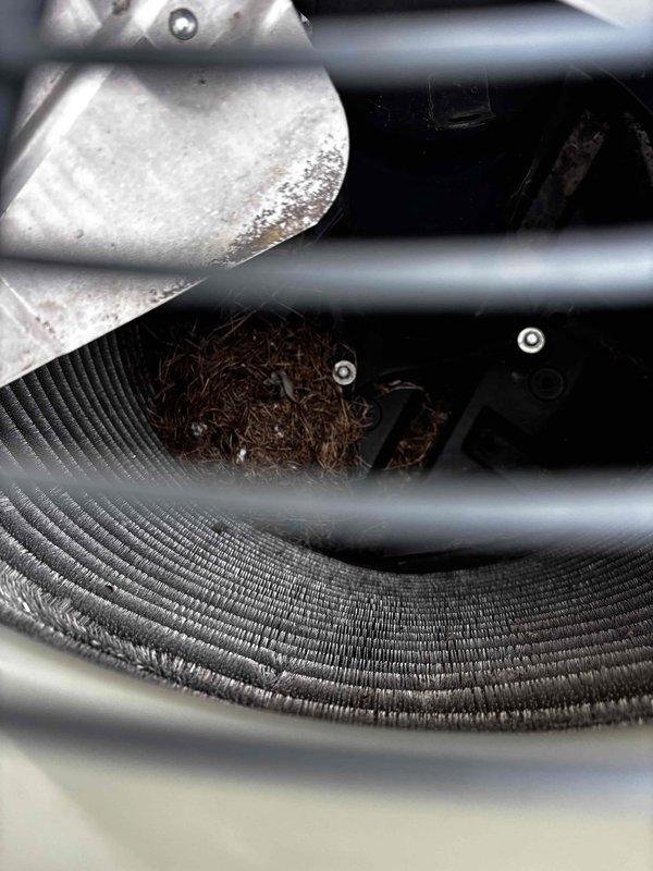 Completed annual cooling maintenance on 12-year-old Trane system. Inspected condenser unit and found debris accumulation including organic material and plant matter lodged between evaporator coils and refrigerant lines. Removed foreign material from interior cavity to restore proper airflow and prevent potential system efficiency loss. Verified fan motor operation, inspected fan guard assembly and housing integrity. All components found to be in functional condition following cleaning. System operational and ready for cooling season.