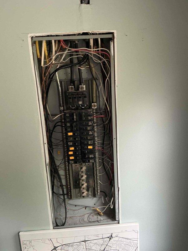 Responded to customer report of refrigerator causing electrical shock when touched. Upon inspection, discovered the dedicated refrigerator outlet lacked proper grounding conductor and exhibited a discolored neutral wire (brown instead of white), indicating potential overheating or age-related deterioration. Inspected main electrical panel to assess overall system condition and grounding infrastructure. Documented panel configuration showing multiple circuit breakers across two vertical bus bars with various branch circuits. Observed mixed wire gauging and color coding throughout panel, consistent with additions made over time. Photographed panel interior showing wire routing, breaker arrangement, and main disconnect components for reference. Identified potential safety concerns requiring immediate attention: absence of equipment grounding conductor at refrigerator outlet poses shock hazard, and discolored neutral wire suggests compromised conductor integrity that could lead to overheat