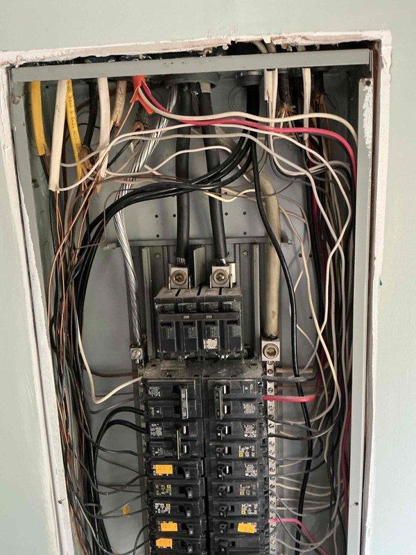 Responded to customer report of refrigerator causing electrical shock when touched. Upon inspection, discovered the dedicated refrigerator outlet lacked proper grounding conductor and exhibited a discolored neutral wire (brown instead of white), indicating potential overheating or age-related deterioration. Inspected main electrical panel to assess overall system condition and grounding infrastructure. Documented panel configuration showing multiple circuit breakers across two vertical bus bars with various branch circuits. Observed mixed wire gauging and color coding throughout panel, consistent with additions made over time. Photographed panel interior showing wire routing, breaker arrangement, and main disconnect components for reference. Identified potential safety concerns requiring immediate attention: absence of equipment grounding conductor at refrigerator outlet poses shock hazard, and discolored neutral wire suggests compromised conductor integrity that could lead to overheat