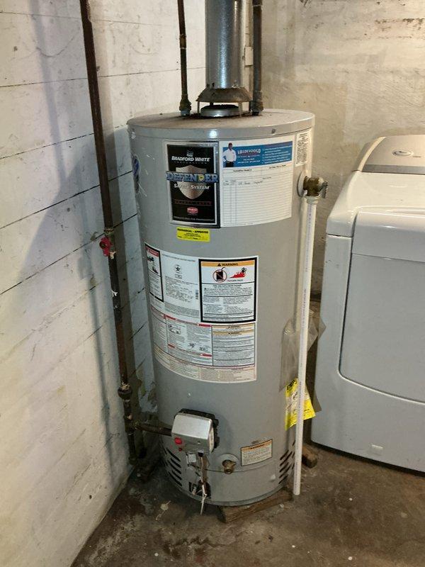Completed on-site assessment of existing water heater installation in basement utility area. Documented current unit specifications, venting configuration with metallic exhaust ductwork, plumbing connections including shut-off valves and piping, and overall installation conditions. Photographed equipment labels, surrounding infrastructure, and workspace layout to provide comprehensive estimate for water heater replacement.