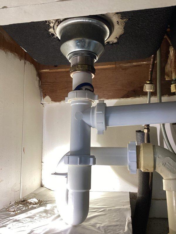 Responded to a leak at kitchen sink. Upon inspection, found the white PVC P-trap assembly beneath the sink had loose compression fittings causing water seepage. Tightened all slip joint connections on the P-trap assembly and verified proper seal at the metal sink drain coupling. Tested the drain system by running water through the sink to confirm leak was resolved and all connections remained dry under pressure.