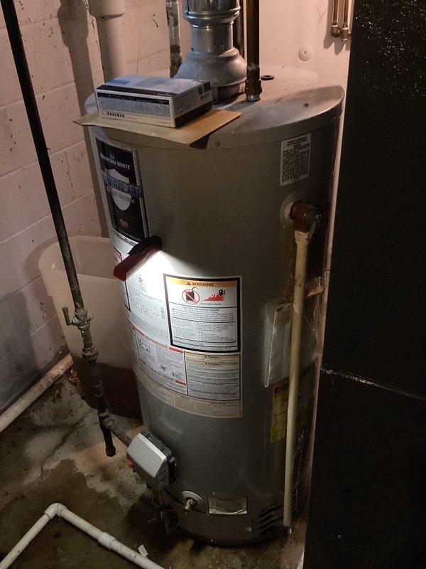 Conducted on-site evaluation of existing residential water heater system located in basement utility area. Documented current equipment configuration including cylindrical tank-style water heater with associated plumbing connections, copper supply lines, PVC drainage piping, and water treatment unit mounted on top of tank. Assessed condition of flexible metal ductwork showing dust accumulation and evaluated overall mechanical room setup. Provided comprehensive estimate for water heater replacement options based on current installation requirements and existing infrastructure.