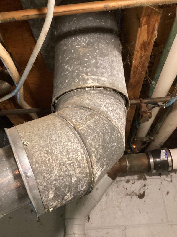 Conducted on-site evaluation of existing residential water heater system located in basement utility area. Documented current equipment configuration including cylindrical tank-style water heater with associated plumbing connections, copper supply lines, PVC drainage piping, and water treatment unit mounted on top of tank. Assessed condition of flexible metal ductwork showing dust accumulation and evaluated overall mechanical room setup. Provided comprehensive estimate for water heater replacement options based on current installation requirements and existing infrastructure.