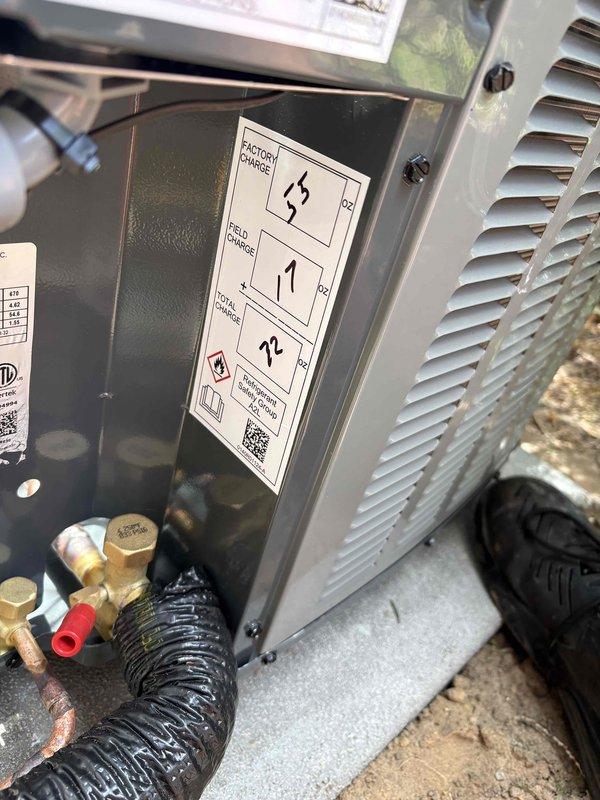 Completed full installation of new furnace and air conditioning system at residential property. Outdoor condensing unit installed on concrete pad against exterior wall with proper clearances for airflow and maintenance access. Electrical disconnect box mounted to building with flexible conduit providing power connection to unit. Refrigerant lines, copper piping, and brass fittings connected and secured at condensing unit base. All manufacturer labels, wiring diagrams, and safety placards properly affixed to equipment. System installed per manufacturer specifications and local code requirements with appropriate clearance from surrounding vegetation.