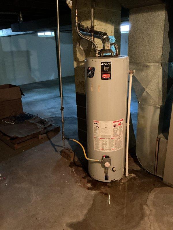 Responded to emergency call for leaking water heater with active water discharge onto basement floor. Upon arrival, found aging water heater with severe corrosion at base and extensive rust damage causing primary leak. Shutoff valve had also begun leaking after attempted closure by occupant. Assessed unit condition, documented extensive water damage on concrete floor surrounding heater, and photographed corroded tank base and failed shutoff valve. Provided estimate for complete water heater replacement including new shutoff valve installation in standard residential foundation basement setting.