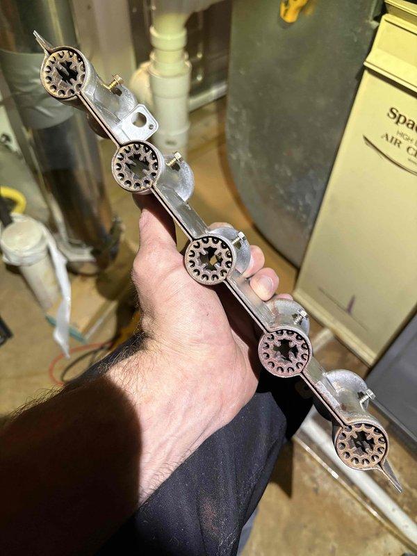 Completed comprehensive furnace tune-up with expanded evaluation of air conditioning system and thermostat per customer request. Performed full system diagnostics on heating and cooling equipment, identifying flame sensor requiring cleaning or replacement and burner assembly showing signs of oxidation and wear. Removed and inspected flame sensor rod assembly with ceramic insulator, finding carbon buildup affecting proper flame detection. Extracted and examined five-port burner manifold assembly, noting corrosion on burner heads that could impact combustion efficiency and flame pattern. Cleaned all burner ports and flame sensor to restore proper operation. Verified gas pressure, ignition sequence, and flame characteristics across all burner heads. Tested thermostat communication with HVAC system to ensure proper heating and cooling calls. Evaluated air handler operation and airflow throughout system. Inspected condensate drainage, electrical connections, and safety controls. System rest