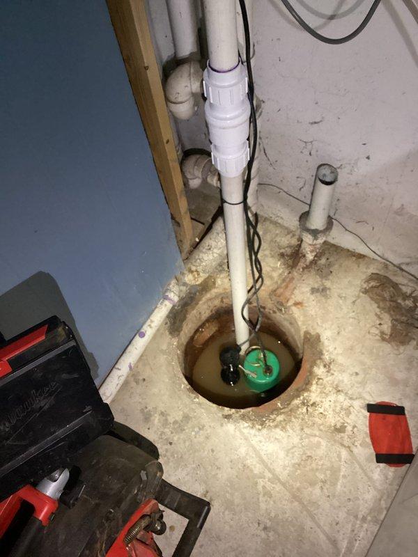 Performed video camera inspection of residential drain line per customer request due to suspected blockage from debris, roots, and foreign material. Accessed drainage system through basement floor drain adjacent to existing sump pump installation. Documented current condition of basement plumbing infrastructure including sump pump basin, discharge piping, and floor drain assembly showing signs of age, mineral deposits, and debris accumulation around drain opening.