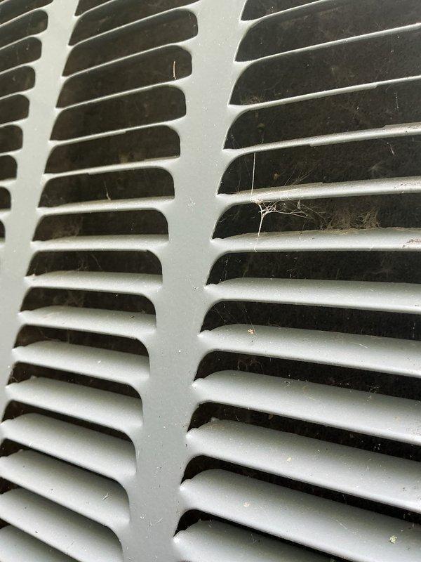 Completed annual cooling maintenance on residential air conditioning system. Removed significant accumulation of leaves and organic debris from condenser unit's top grille and surrounding area. Cleaned outdoor unit exterior surfaces, removing dirt and weathering buildup from metal casing. Inspected and cleaned return air vent grille, addressing dust accumulation and cobweb buildup between louvers. Performed standard AC tune-up procedures including system performance verification. Unit operational and ready for cooling season.