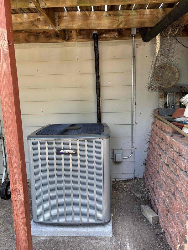 Completed add-on air conditioning system installation at residential property. Installed new gray condenser unit on concrete pad against exterior wall with proper refrigerant line set, electrical disconnect box, and metal conduit for power supply. All refrigerant lines properly insulated with black flexible insulation wrapping, system tested and operational.