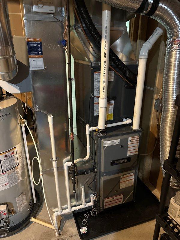 Completed full residential HVAC system installation including new Amana furnace and outdoor AC condenser unit. Furnace installed in interior mechanical room with proper venting using white PVC piping, connected to existing ductwork infrastructure, and integrated with water heater utilities. Outdoor condenser unit positioned on concrete pad against exterior wall with appropriate clearances, electrical disconnect box mounted, refrigerant lines and conduit properly routed through siding. All equipment secured, tested for proper operation, and system commissioned to manufacturer specifications.