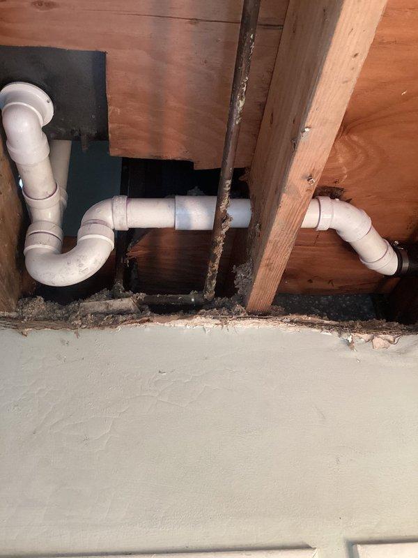 Rebuilt drain line system beneath dual sink installation, replacing deteriorated drainage components with new white PVC piping and P-trap assemblies on both left and right sides. Properly configured trap sections to code specifications, secured all pipe connections through floor joists, and ensured proper slope for drainage while maintaining sewer gas barriers.