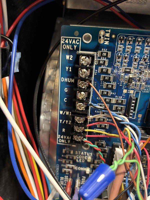 Responded to service call for Amana AC system displaying thermostat error code N260 indicating low voltage issue. Upon arrival, verified AC system was operational despite error code on 10-year-old unit. Inspected thermostat wiring at wall-mounted base and traced connections to control board terminals. Examined circuit board terminal connections including R, C, G, Y1, Y2, W1, W2, DHUM, and OB terminals to verify proper 24VAC supply and wiring integrity. Photographed thermostat base wiring configuration showing yellow, orange, pink, green, blue, and white conductors, and documented control board terminal connections. Tested voltage at thermostat and control board to identify source of low voltage condition. Confirmed all wire connections were secure at both thermostat mounting base and HVAC control board terminals. Cleared error code and restored normal thermostat operation.
