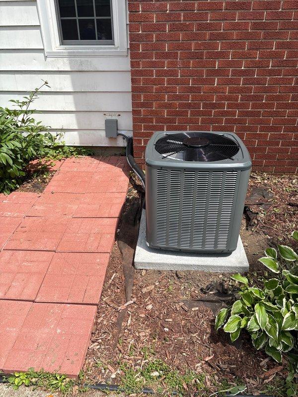 Completed full air conditioning system replacement including outdoor condenser unit and indoor air handler. Installed new gray cylindrical condenser unit on concrete pad with proper electrical disconnect and conduit routing, positioned adjacent to building exterior between vinyl siding and brick sections. Indoor installation included dark-colored furnace/air handler unit in basement utility area with metal supply ductwork, flexible return ducting, and condensate management system with drain pan. All electrical connections, refrigerant lines, and drainage systems installed per manufacturer specifications and verified operational.