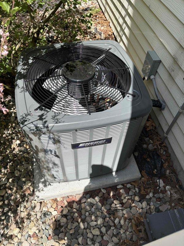 Completed full installation of new furnace and air conditioning system. Interior furnace unit installed in wooden cabinet enclosure with proper venting via white PVC piping, gas valve assembly connected, electrical wiring completed, and metal ductwork integrated with existing plenum. Exterior condensing unit positioned on concrete pad against building exterior with appropriate clearances, electrical disconnect box mounted to siding, and unit leveled and secured. All refrigerant lines connected, system charged, tested for proper operation, and verified all safety controls functioning correctly.