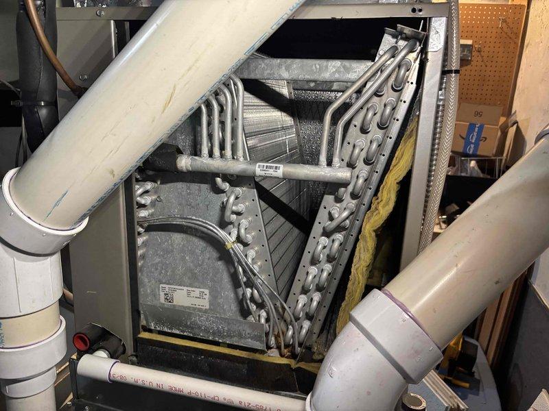 Responded to water leak complaint above furnace in mechanical room. Upon inspection, identified condensate drainage issue from evaporator coil assembly on 22-year-old Carrier HVAC system. Documented equipment condition with photographs showing heat exchanger coil configuration and interior ductwork with insulation. Assessed drainage system and provided findings to customer for necessary repairs.