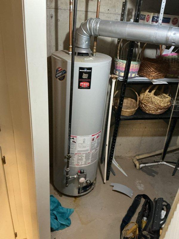 Responded to water heater leak complaint and found a 25+ year old residential water heater with a slight trickle leak in basement utility room. Upon inspection, documented the aging unit with multiple deteriorated components and evidence of moisture on the concrete floor near the base. Given the advanced age of the equipment (exceeding typical 10-15 year lifespan) and active leak condition, recommended complete water heater replacement to prevent potential flooding and property damage.