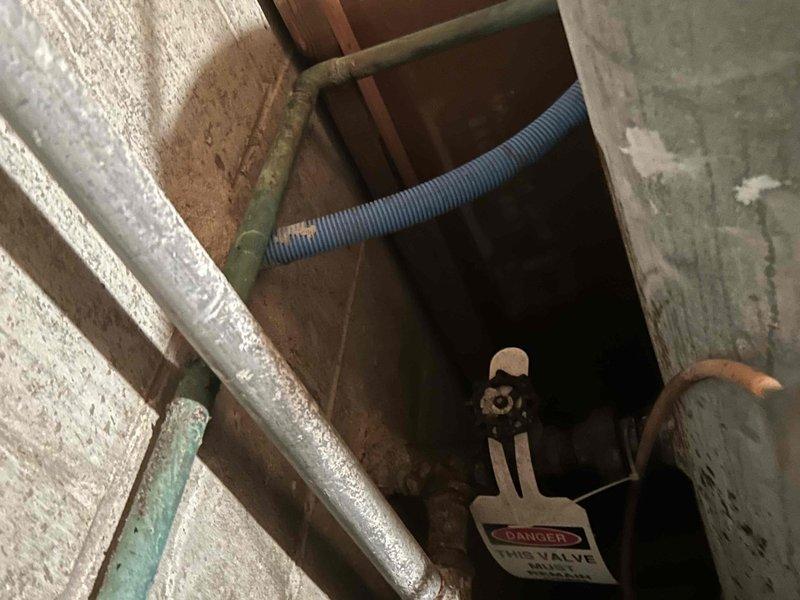 Responded to report of outside spigot leaking with visible water running and squirting from single location, noticed after sprinkler system activation. Upon arrival, inspected exterior hose bib and traced supply lines into basement utility area of 1972-built home. Located main water supply piping system with multiple copper lines showing age-related patina and corrosion. Identified shutoff valves serving exterior fixtures and documented existing plumbing configuration with aged copper supply lines, green-handled isolation valves, and various branch connections throughout exposed basement ceiling joists. Photographed plumbing infrastructure including insulated supply lines, flexible connections, and lockout-tagged equipment for service documentation. Customer reported concurrent issues with low pressure in certain sprinkler zones and non-functioning water softener, though stated belief that exterior leak was not irrigation-system related.