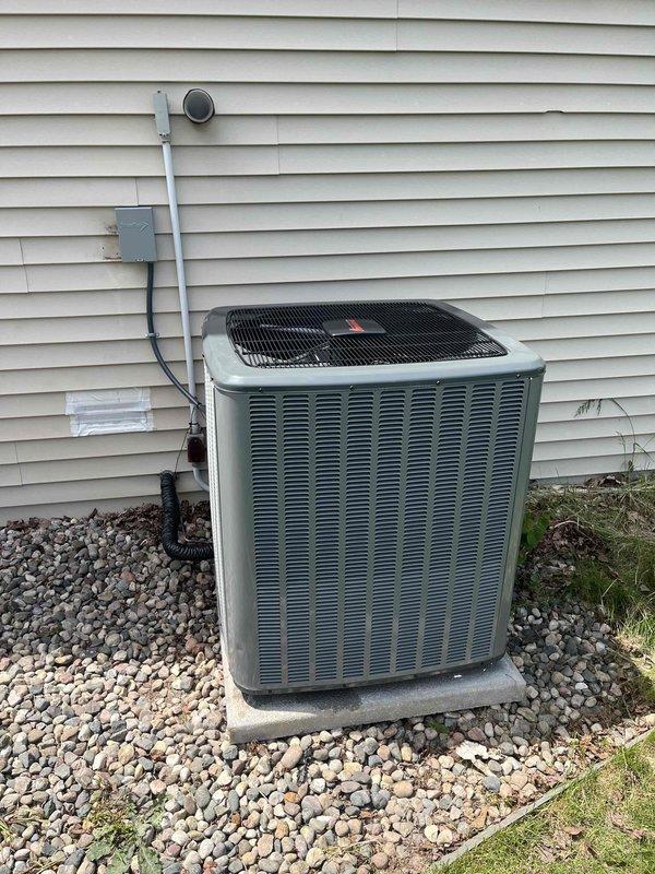 Completed full air conditioning system replacement at residential property. Removed existing outdoor condensing unit and installed new replacement unit on existing concrete pad with river rock base against exterior wall. Unit positioned on stable foundation with proper clearances for airflow and service access. Ran electrical conduit to weatherproof junction box mounted on exterior wall and connected power supply per manufacturer specifications. Installed refrigerant line set with protective conduit covering along wall. Verified all electrical connections secure and properly grounded. Completed refrigerant charging and pressure testing of system. Performed startup procedures and confirmed proper operation of compressor and condenser fan motor. Verified airflow through condenser coil and checked for proper cycling. System operating within normal parameters with all safety controls functioning correctly. Installation meets manufacturer requirements and local code standards.
