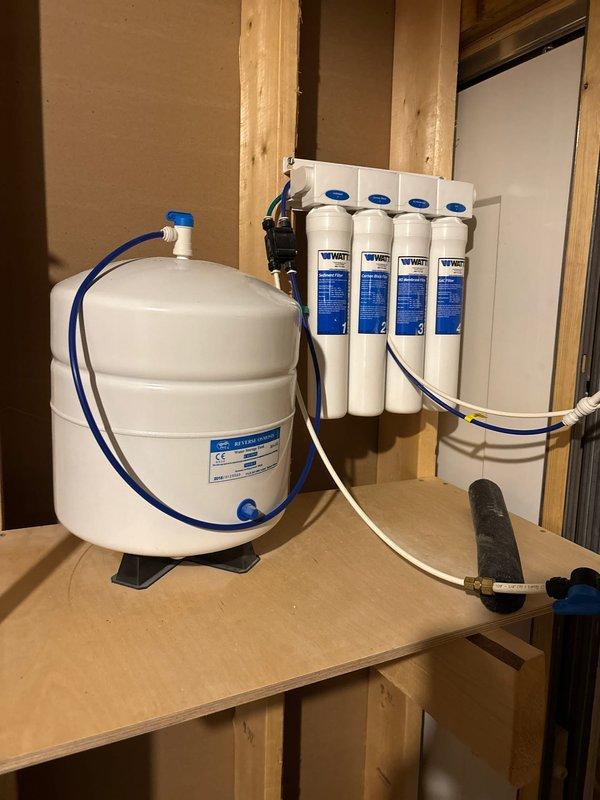 Responded to complaint of continuous water running sound in kitchen drain. Diagnosed issue as faulty reverse osmosis system with water bypassing storage tank and draining directly into drain line. Isolated problem by shutting off water supply to RO unit, which eliminated the sound. Inspected four-stage filtration system and pressurized storage tank, verified proper connections and tubing routing, and restored normal operation to the reverse osmosis unit.
