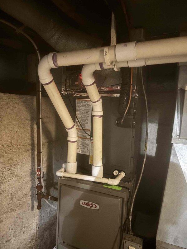 Successfully completed full air conditioning system replacement at residential property. Installed new Lennox furnace unit in basement utility area with comprehensive PVC condensate drain and venting system configuration. Routed copper refrigerant lines from indoor unit to exterior. Positioned new outdoor condenser unit on concrete pad against exterior wall with proper clearances. Installed gray PVC electrical conduit, disconnect box, and completed all electrical connections to meet code requirements. System tested and verified operational upon completion.