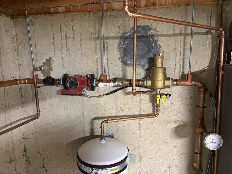 Responded to low water pressure complaint and performed comprehensive diagnostic evaluation of residential hydronic heating system and domestic water supply. Upon inspection, identified and assessed circulator pump operation, pressure reducing valve assembly, zone valves, expansion tank, and system pressure gauge mounted on basement mechanical room wall. Verified proper function of all heating system components including boiler unit, copper distribution piping, isolation valves, and circulation equipment. Documented existing system configuration with photos showing complete installation layout and component arrangement for service records.