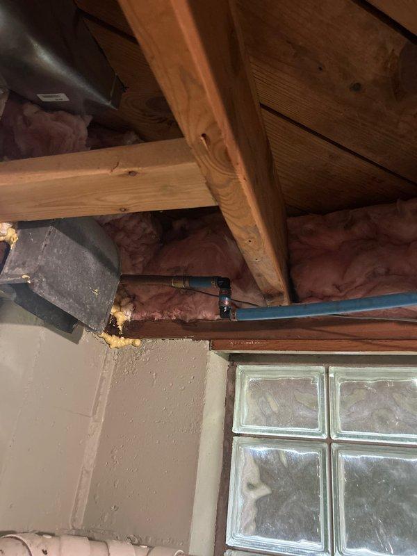 Responded to plumbing leak at outdoor spigot where water was leaking between the valve and exterior wall connection. Inspected interior piping in attic space and traced copper water lines to the exterior hose bib, then examined the outdoor faucet with red protective cover and identified the source of the leak at the connection point. Documented conditions with photos showing interior plumbing configuration and exterior fixture with visible water staining on concrete surface below the spigot.