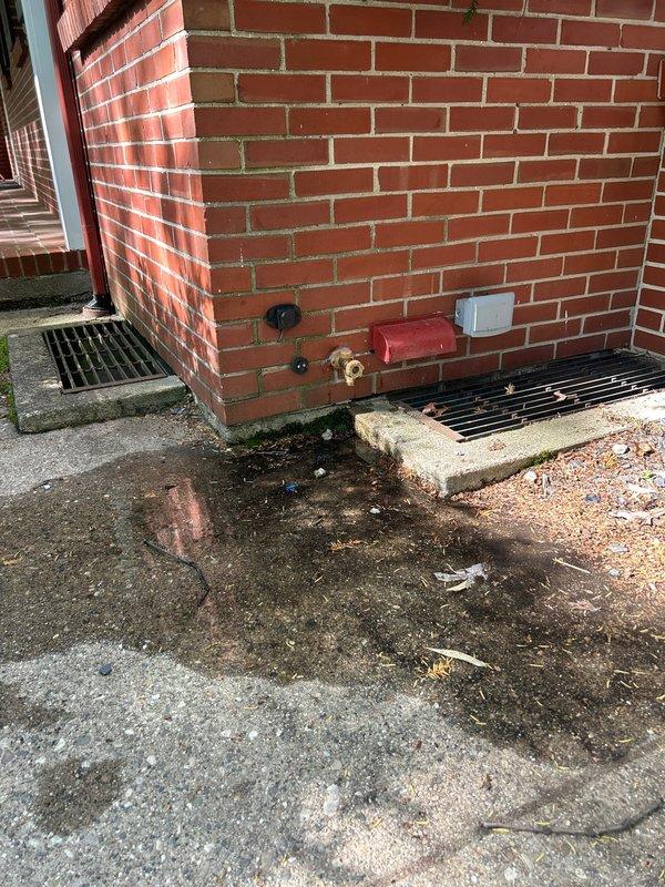 Responded to plumbing leak at outdoor spigot where water was leaking between the valve and exterior wall connection. Inspected interior piping in attic space and traced copper water lines to the exterior hose bib, then examined the outdoor faucet with red protective cover and identified the source of the leak at the connection point. Documented conditions with photos showing interior plumbing configuration and exterior fixture with visible water staining on concrete surface below the spigot.