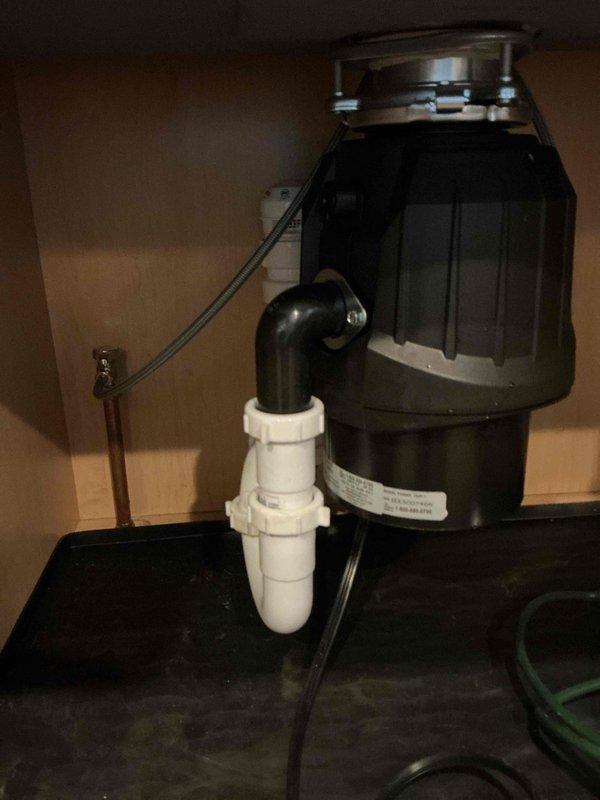 Completed kitchen drain rework for single basin sink configuration with new garbage disposal installation. Reconfigured drain tubular assembly, installed disposal unit with proper mounting flange and hardware, and connected white PVC P-trap to discharge outlet ensuring proper drainage flow and code-compliant installation.