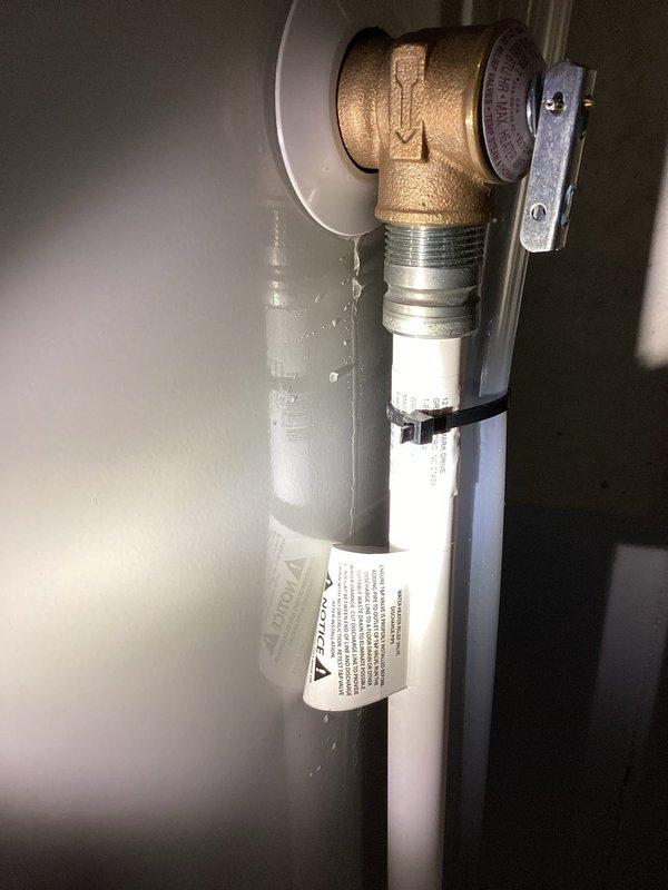 Responded to service call for non-functional and leaking 4-year-old water heater. Upon inspection, identified active leak condition and assessed temperature and pressure relief (TPR) valve assembly and discharge piping system. Examined brass 90-degree elbow fitting, pressure relief valve with gauge, and PVC discharge pipe showing condensation and moisture accumulation indicating recent water flow. Inspected drip pan beneath unit which contained visible water, discoloration, and sediment accumulation consistent with ongoing leak. Documented existing conditions of TPR valve installation, wall-mounted plumbing connections, and water heater base assembly. Assessed galvanized drip pan condition and verified proper positioning beneath appliance to capture discharge water.