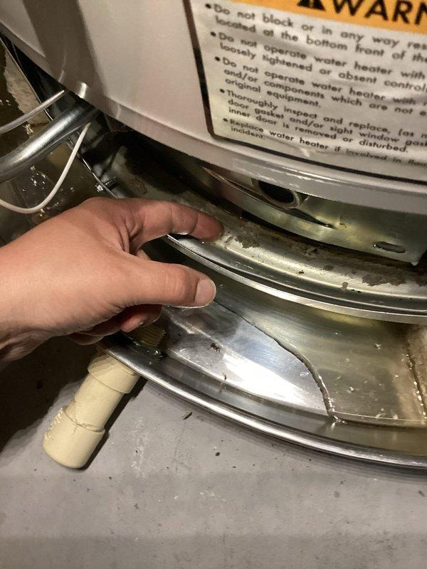 Responded to service call for non-functional and leaking 4-year-old water heater. Upon inspection, identified active leak condition and assessed temperature and pressure relief (TPR) valve assembly and discharge piping system. Examined brass 90-degree elbow fitting, pressure relief valve with gauge, and PVC discharge pipe showing condensation and moisture accumulation indicating recent water flow. Inspected drip pan beneath unit which contained visible water, discoloration, and sediment accumulation consistent with ongoing leak. Documented existing conditions of TPR valve installation, wall-mounted plumbing connections, and water heater base assembly. Assessed galvanized drip pan condition and verified proper positioning beneath appliance to capture discharge water.