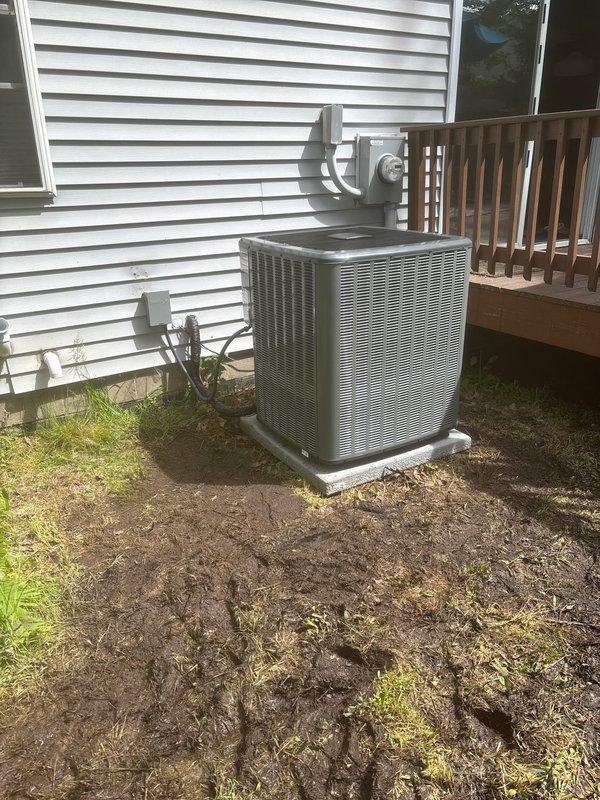 Completed full air conditioning system replacement at residential property. Installed new outdoor condenser unit on concrete pad against exterior wall with proper electrical disconnect box and refrigerant line connections through vinyl siding. System charged with 87 oz factory refrigerant charge per manufacturer specifications, with service valves properly installed and capped for future maintenance access. All electrical conduit and copper refrigerant lines secured to exterior wall, unit positioned for optimal airflow and serviceability adjacent to elevated deck structure.